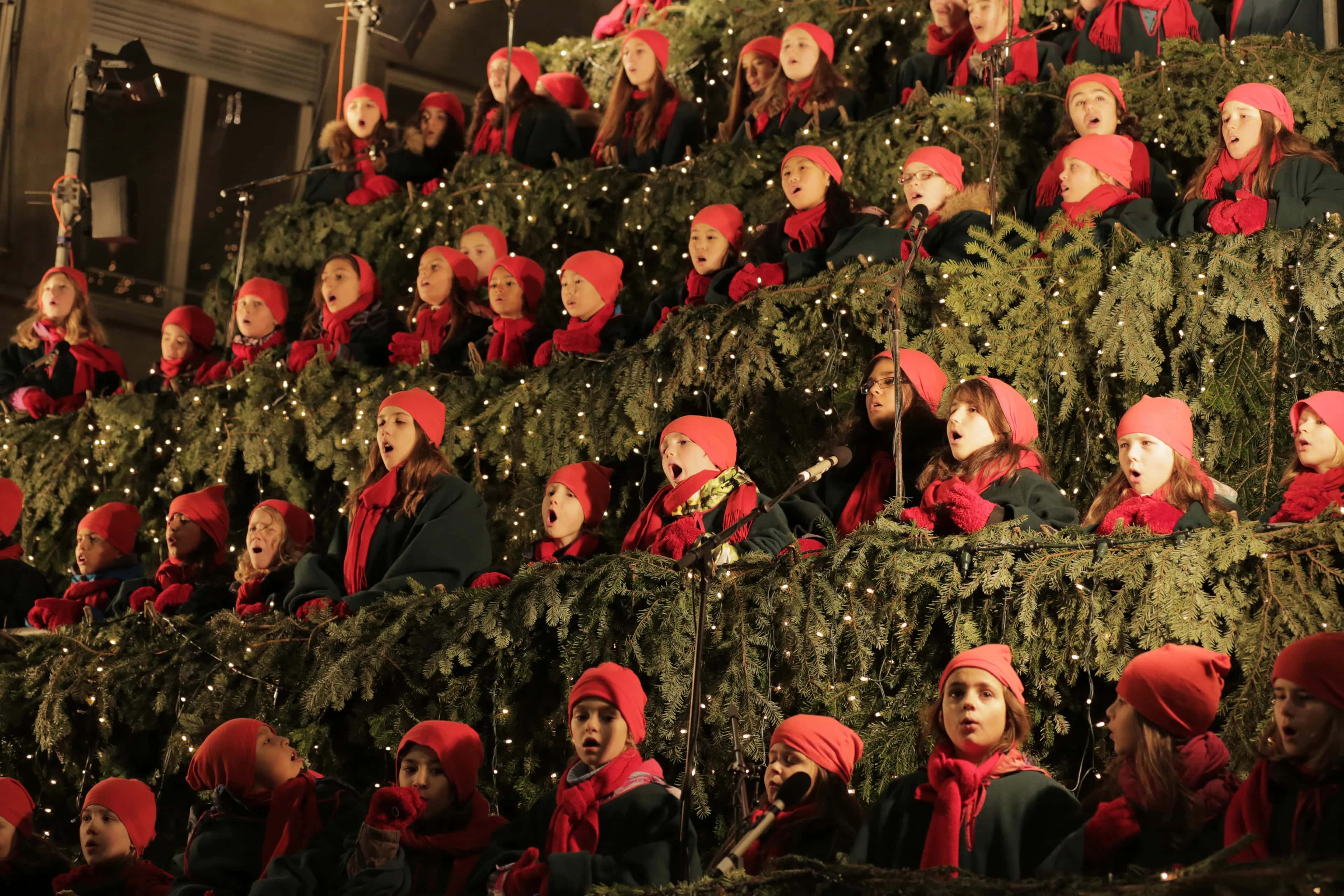 Kinderchor in roten Mützen und Schals singt auf den tannengeschmückten Stufen des Singing Christmas Tree in Zürich